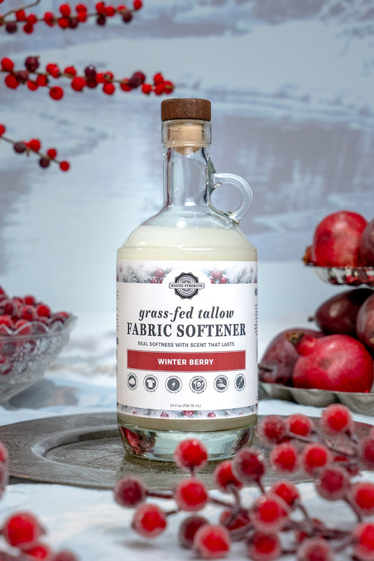 Rustic Strength, bottle of grass-fed tallow fabric softener with a cork stopper, styled on a rustic silver tray with red berries and pomegranates in the background.