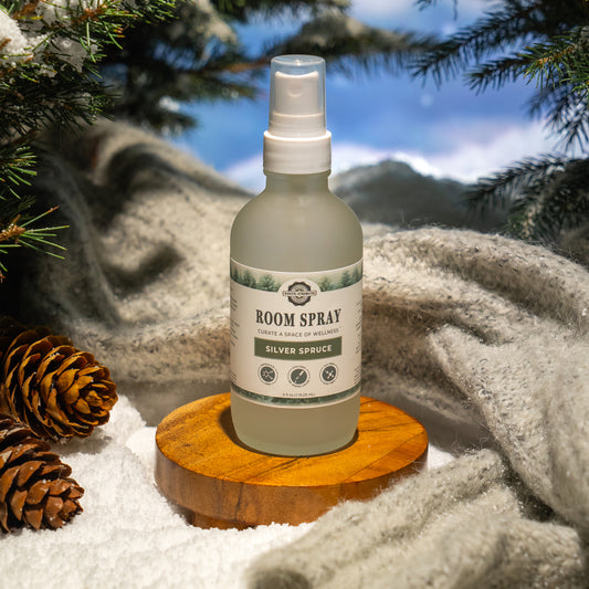 Rustic Strength, Room spray bottle labeled 'Silver Spruce' on a wooden coaster with pinecones and snow in the background