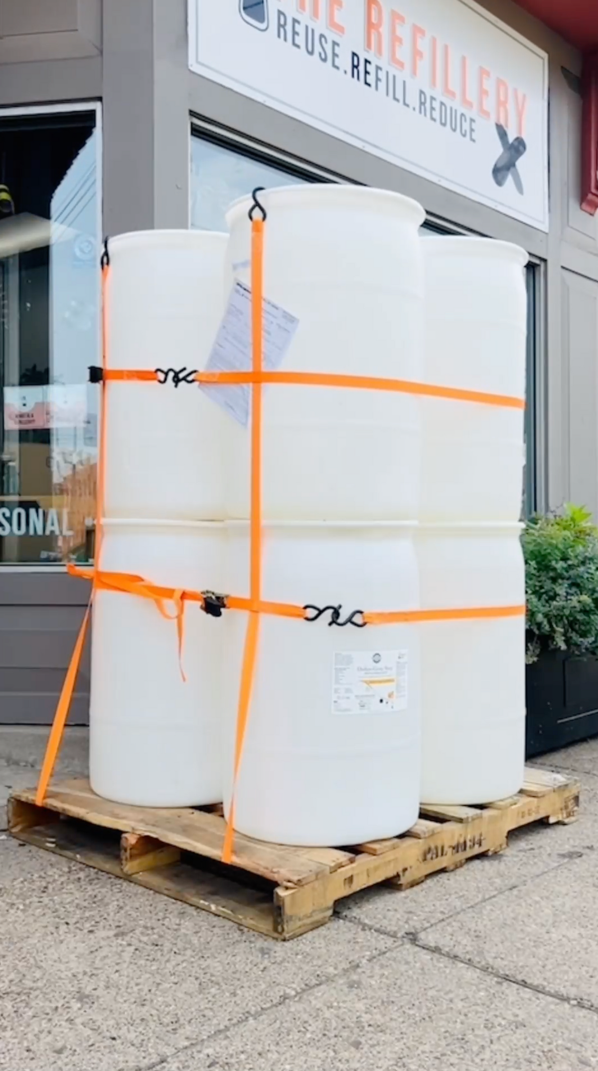 Rustic Strength, Stacked white drums on a pallet with orange straps in front of a store.